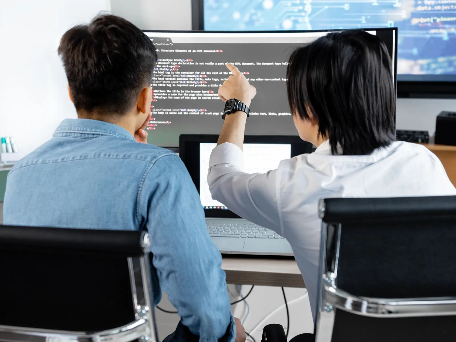 Two colleagues working together on web application code shown on a desktop monitor
